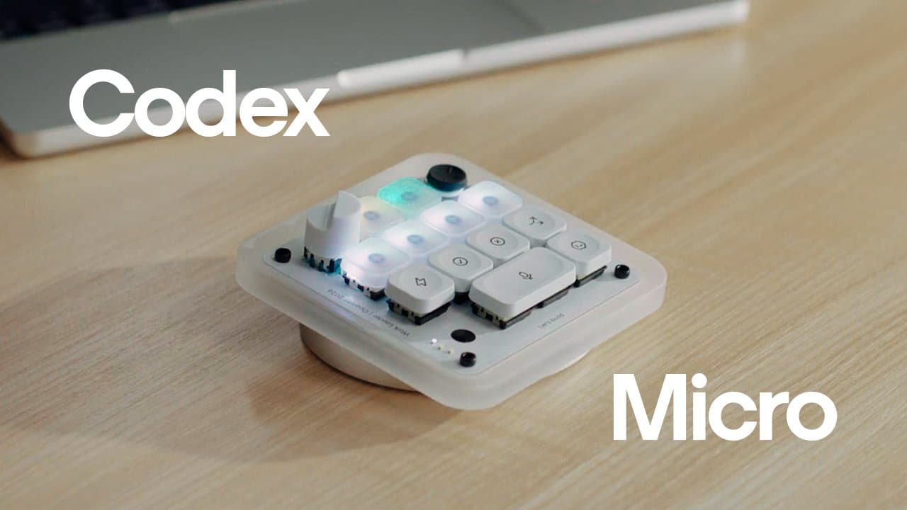 The Codex Micro on a desk — a small translucent macro pad with lit keys, a dial, and a joystick